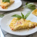 slice of red pepper and potato frittata on a white plate with fresh basil